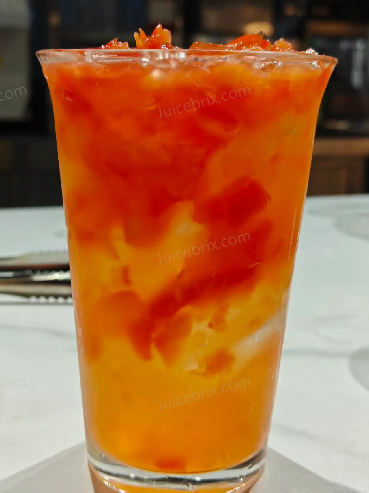 Orange-red bell pepper beverage with ice and visible pepper pieces, prepared during an application trial.